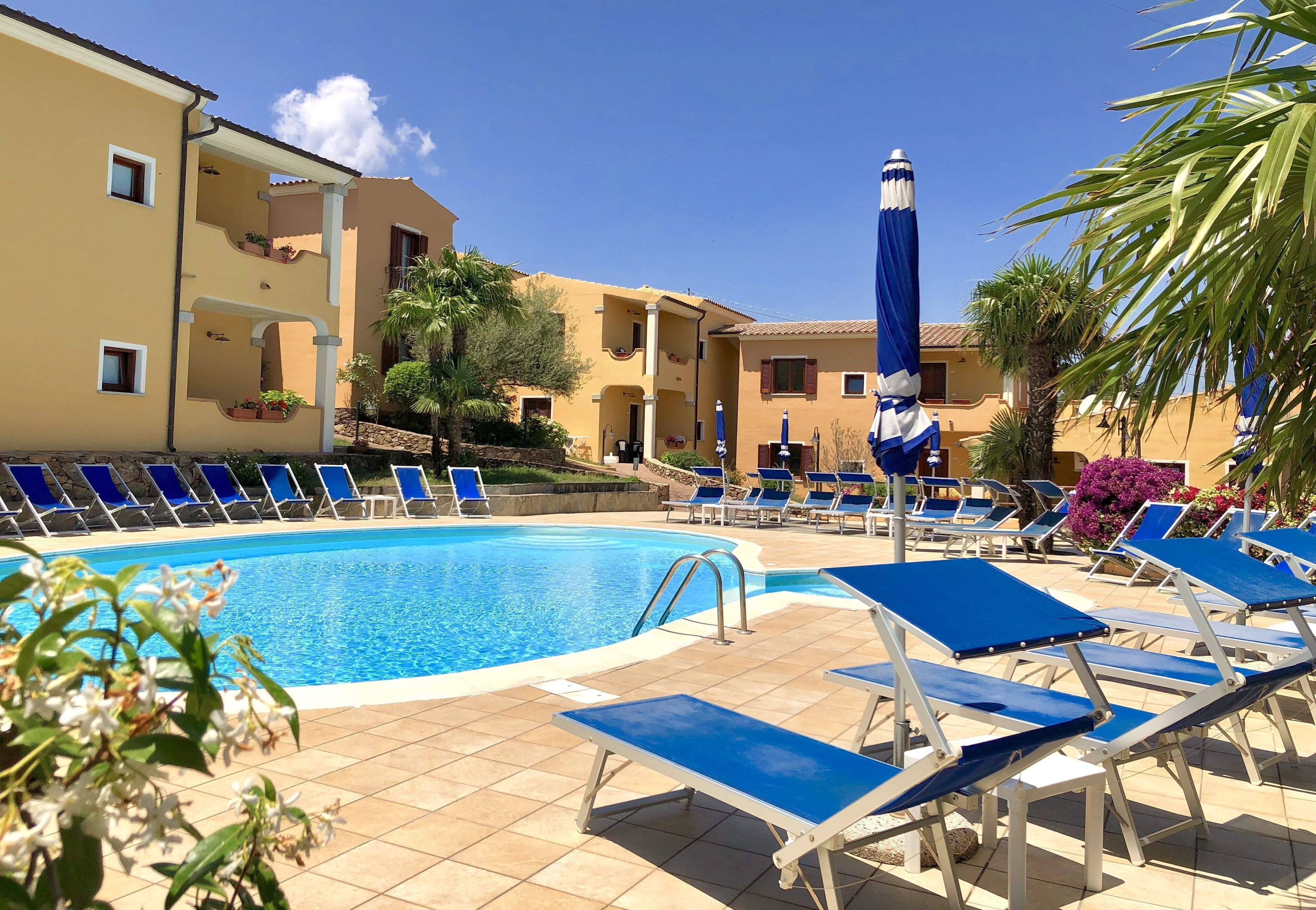 A pool area with blue lounge chairs and a clear blue pool.