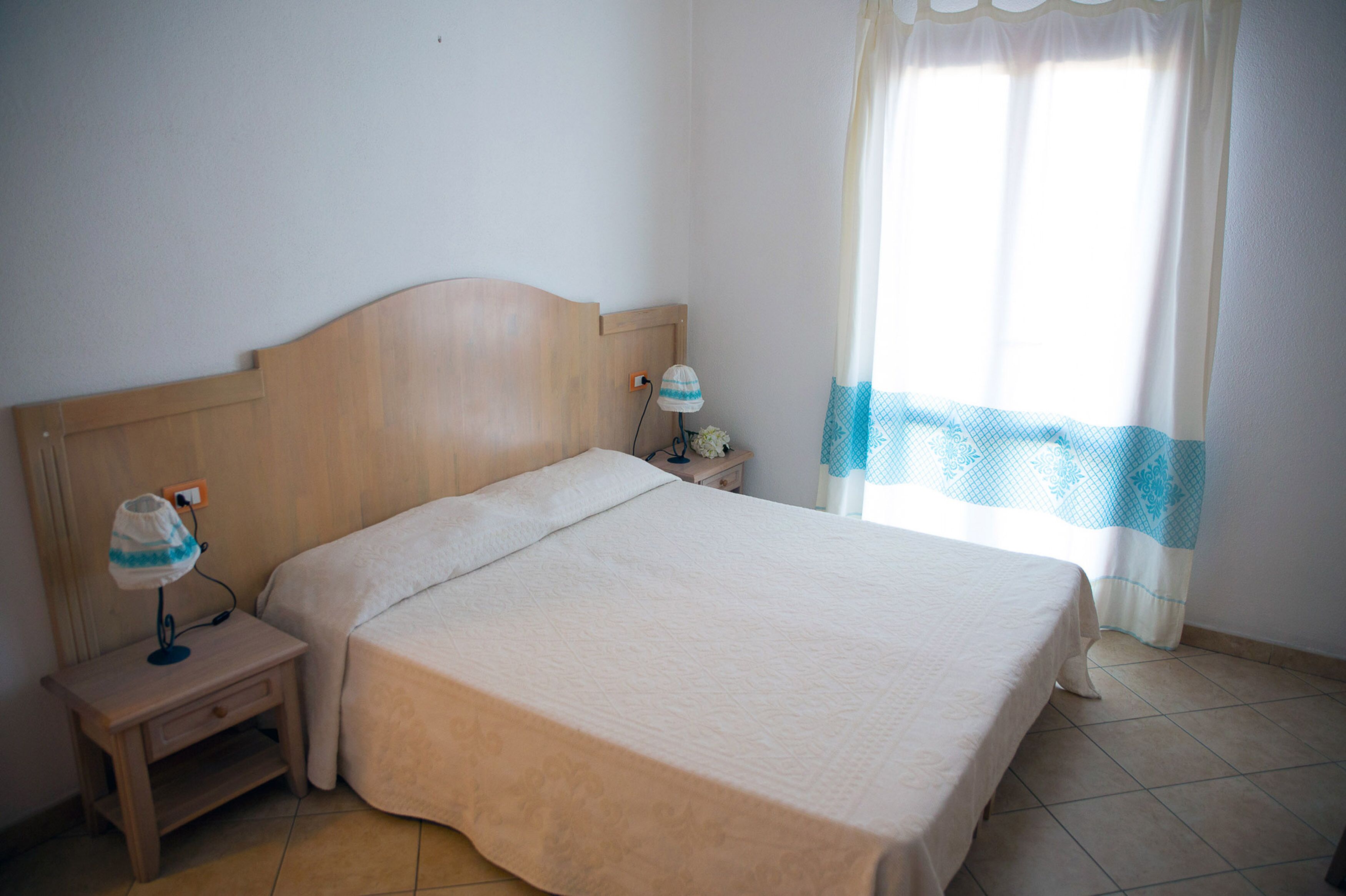 Una cama bien hecha con cabecera de madera, una lámpara de noche y una mesita de noche con lámpara.