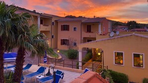 A residential building with multiple balconies, a patio area with lounge chairs, and satellite dishes on the roof. - Residence Corte dei Venti (Budoni)