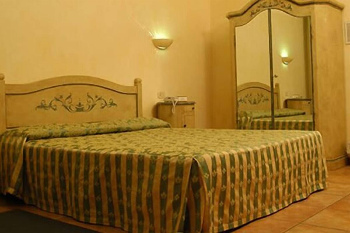 A single bed with a striped bedspread, a nightstand, a mirror, and a wall-mounted light fixture.