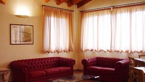 Una sala de estar con dos sofás rojos, una mesa de centro de vidrio y dos ventanas con cortinas color beige.