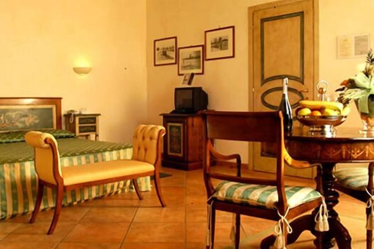 A hotel room with a bed, a wooden chair, a dining table with a fruit bowl, and a television on a wooden cabinet.