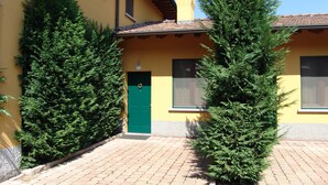 Un edificio amarillo con puerta verde, dos ventanas y una chimenea.