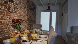 A breakfast table set with croissants, grapes, and a glass of orange juice, with a brick wall and a door in the background. - AppartBrussels (Brussels)