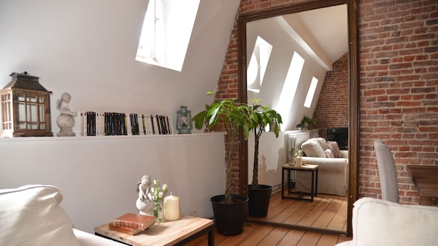 A cozy loft-style room with a sloped ceiling, exposed brick walls, a large mirror, and a wooden floor. - AppartBrussels (Brussels)