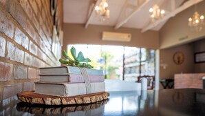 A stack of books on a wooden coaster in a room with a brick wall and a ceiling with exposed beams. - Klip en Kristal Guest House (Bela-Bela)