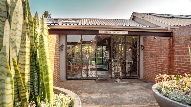 A reception area with a sign reading "ONTVANGS / RECEPTION," a brick wall, metal gates, and potted plants. - Klip en Kristal Guest House (Bela-Bela)