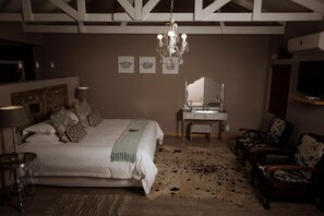 Een slaapkamer met een groot bed, een kaptafel met spiegel, een kroonluchter en een televisie aan de muur.