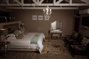 Quarto com cama grande, penteadeira com espelho, lustre e televisão na parede.