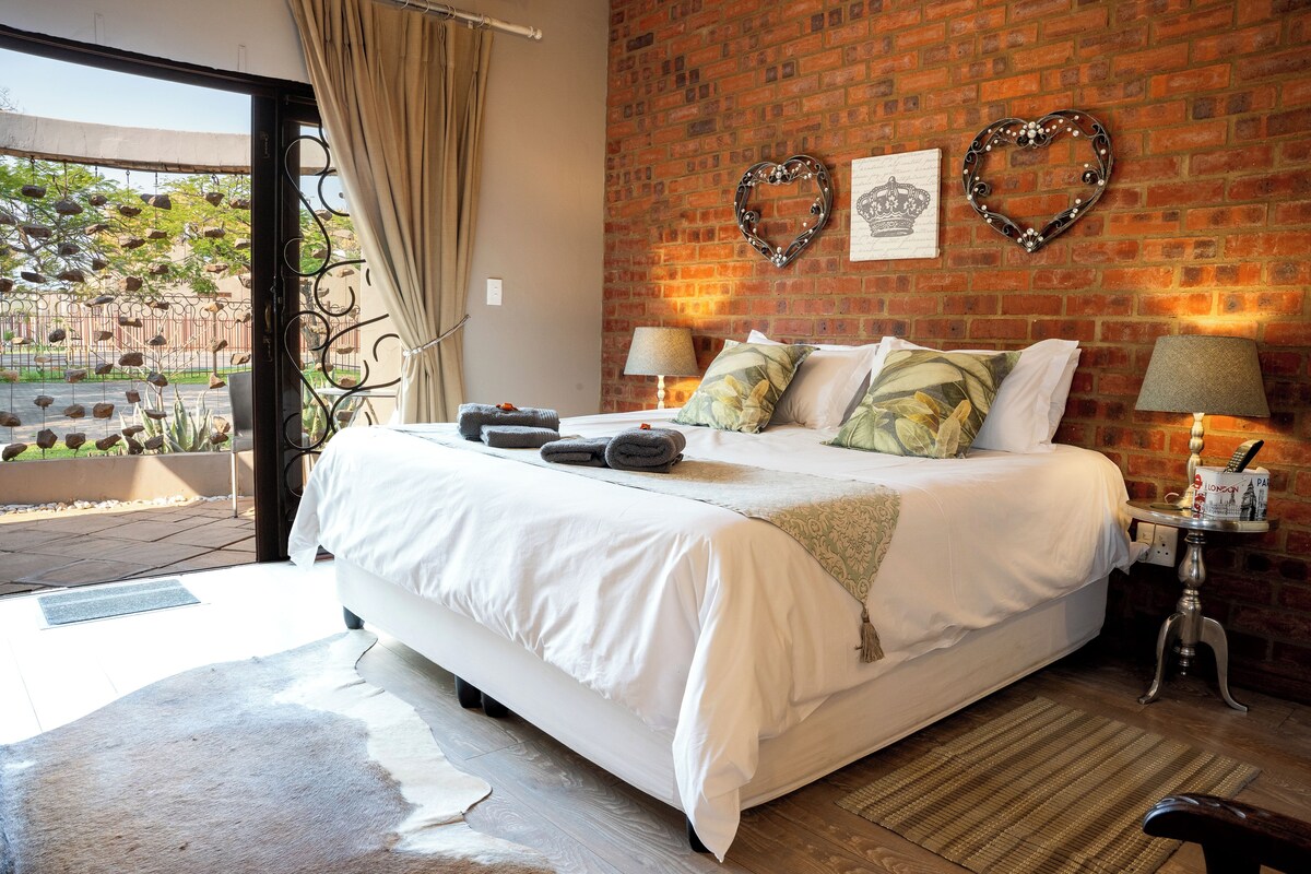 A bedroom with a large bed, a brick wall, two heart-shaped decorations, and a window with curtains.