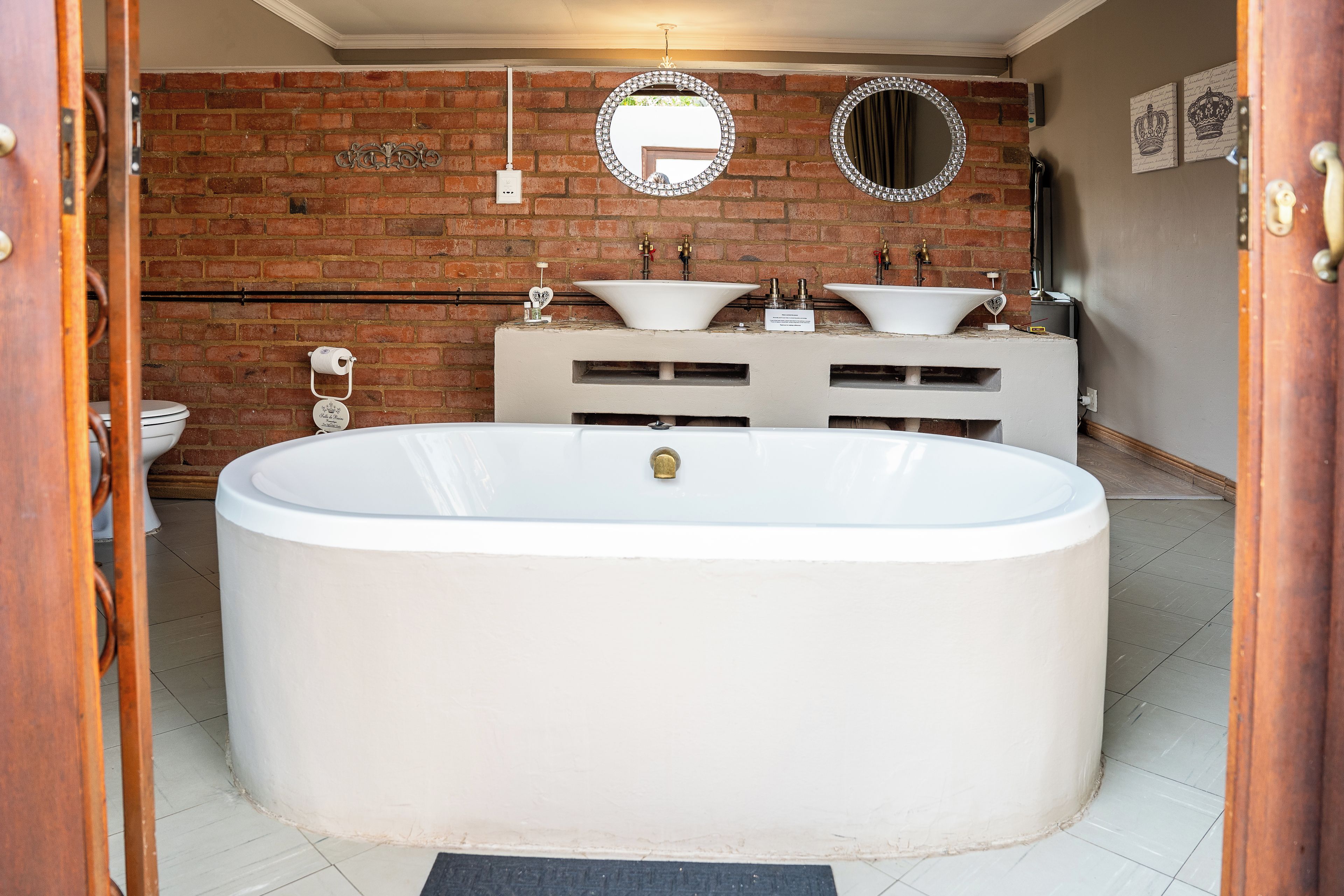A bathroom with a large freestanding bathtub, a double sink vanity, and a brick wall.