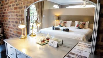 Une chambre d’hôtel avec un grand miroir, un lit avec des oreillers, une table de chevet avec une lampe et une carafe en verre, et un mur en briques.