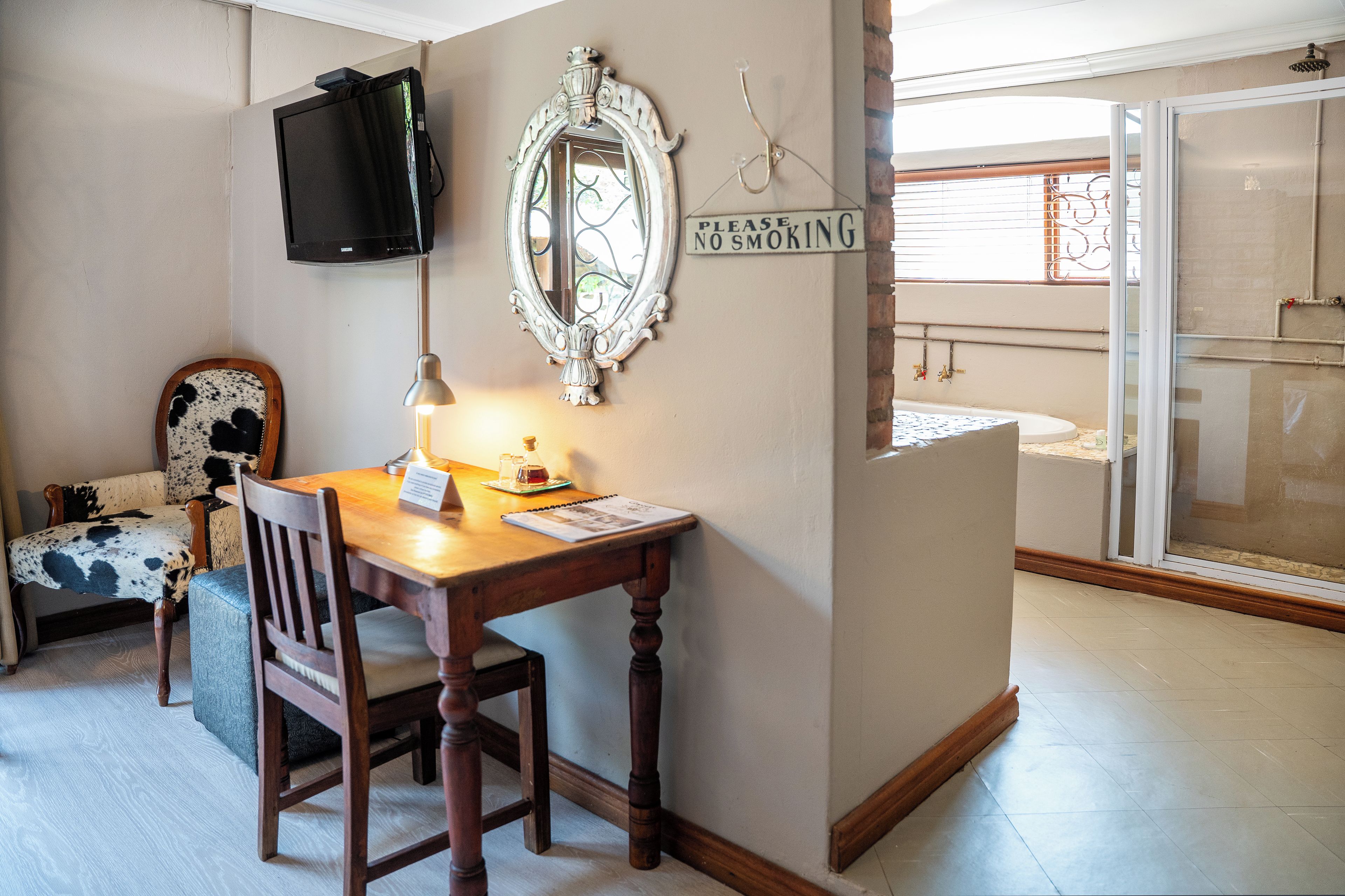A room with a wooden desk, a chair, a television mounted on the wall, a mirror, and a 'Please No Smoking' sign.