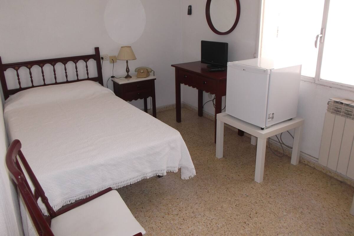 A bedroom with a bed, a desk, a television, and a radiator.