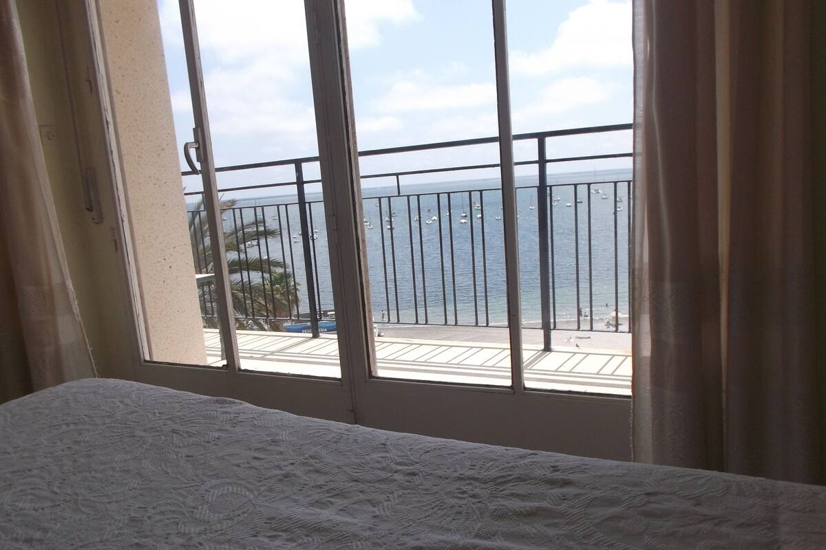 A hotel room with a balcony overlooking a beach and the sea.