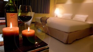 A hotel room with a bed, two lit candles, and a bottle of wine on a table. - Fourteen Again Hotel (Pattaya)