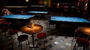 A billiards room with multiple tables, stools, and a central table with a pineapple decoration. - Fourteen Again Hotel (Pattaya)