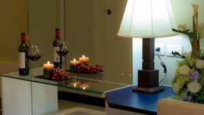A room with a glass-top table, two wine bottles, glasses, candles, a lamp, and a floral arrangement. - Fourteen Again Hotel (Pattaya)