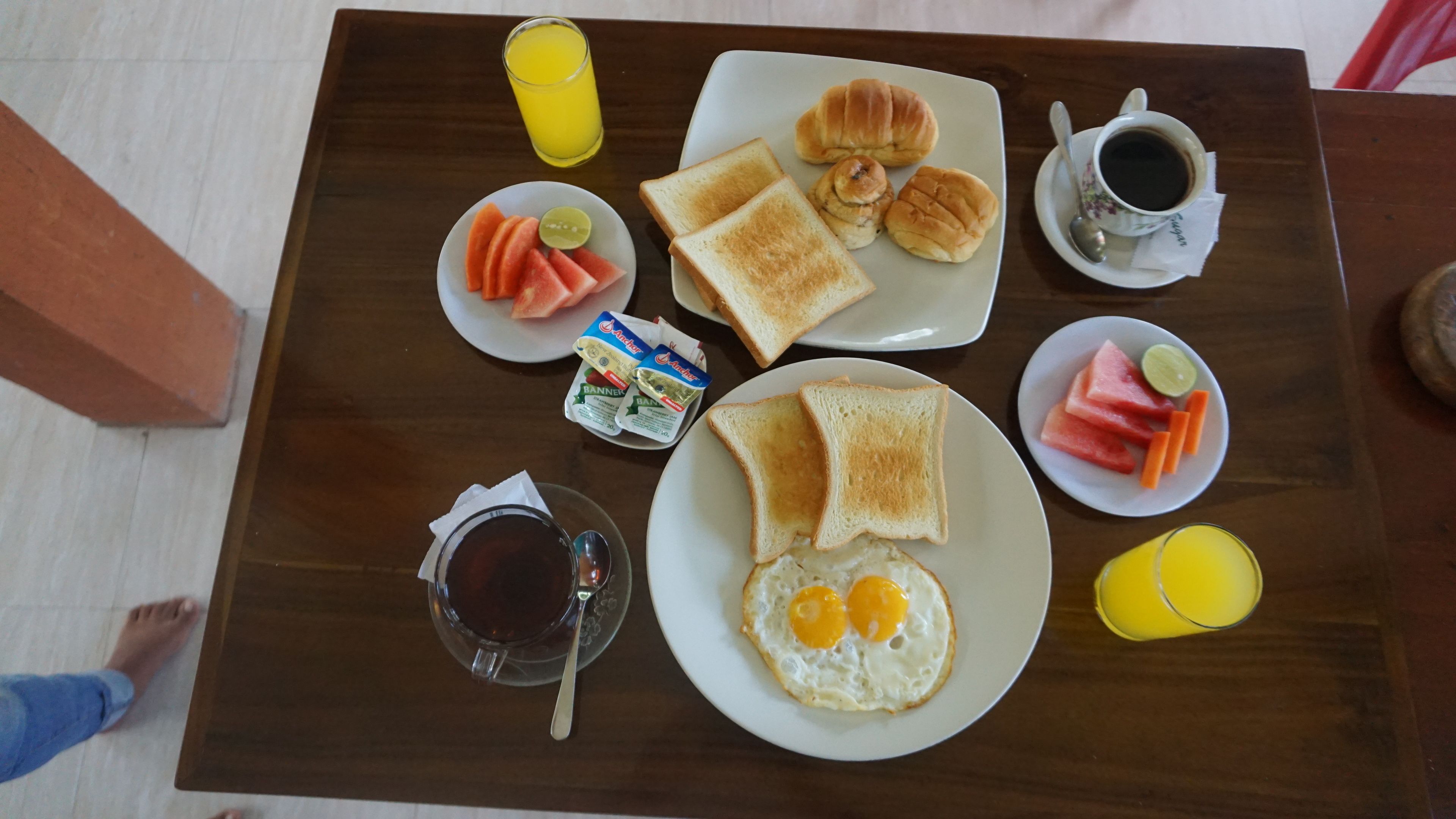 A breakfast tray with toast, croissants, eggs, and fruit on a wooden table.
