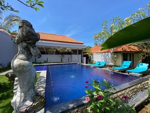 A swimming pool with blue water, surrounded by lounge chairs and a stone statue.