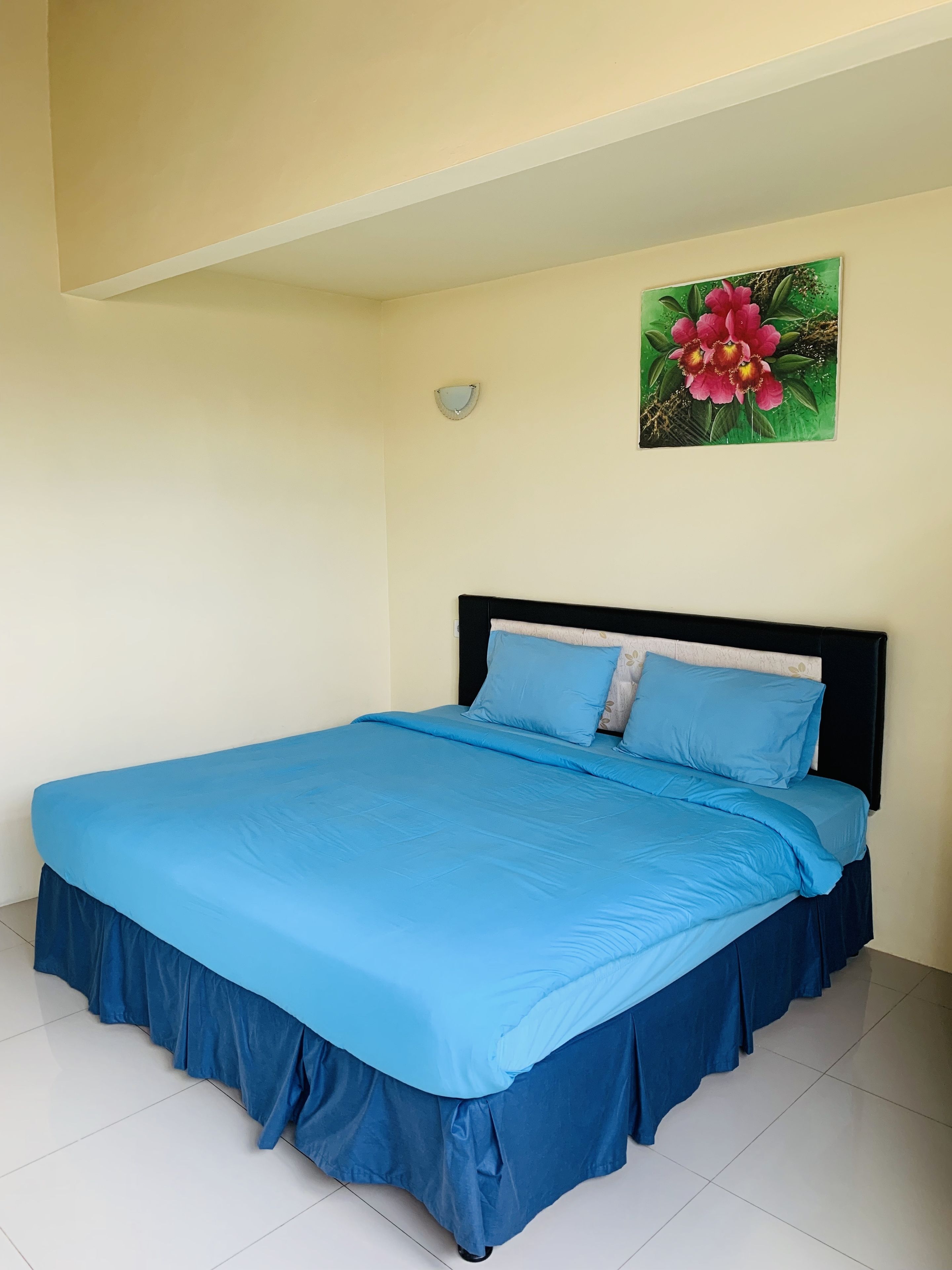 A bed with a blue bedspread and matching skirt, a black headboard, and a wall-mounted light fixture.