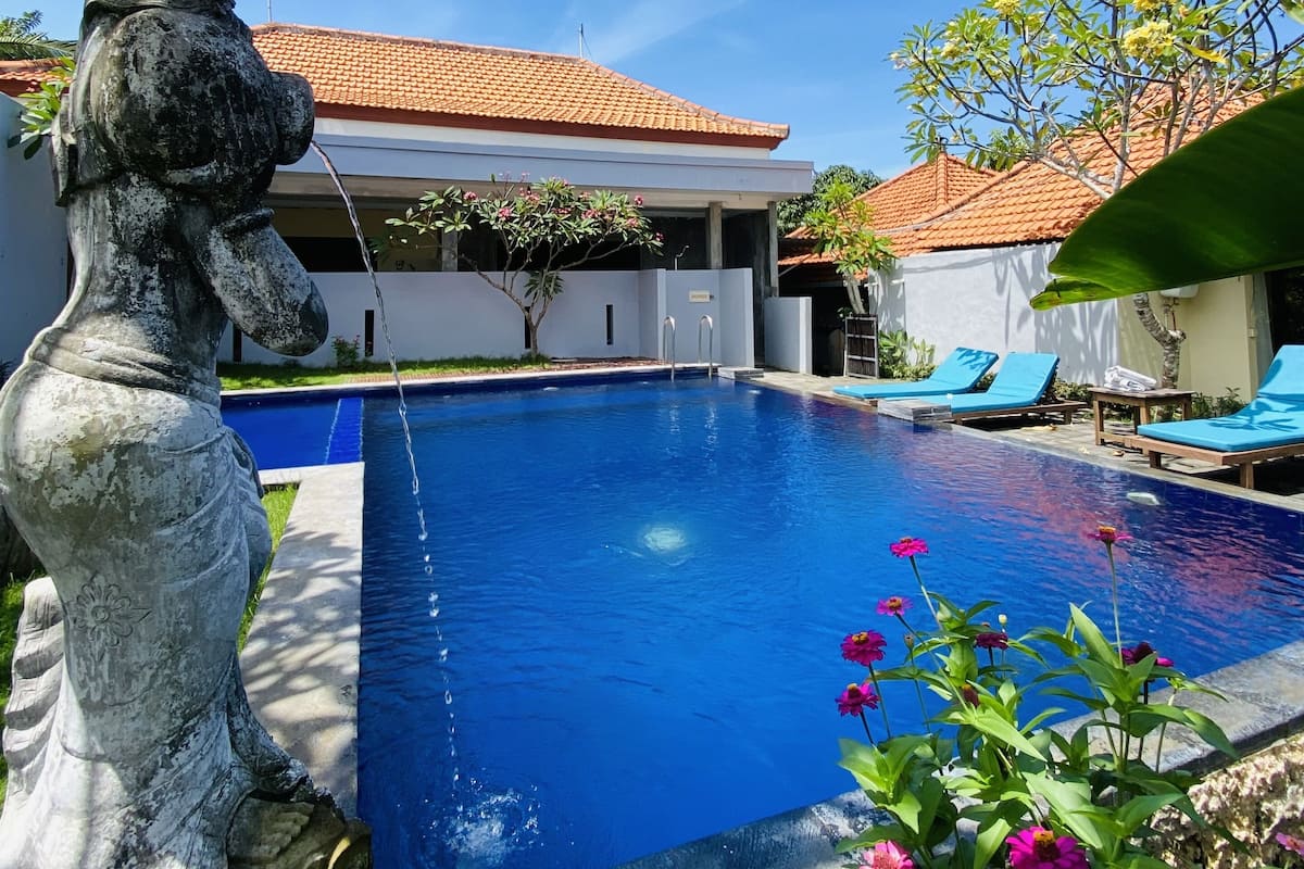 A swimming pool with a statue, a tiled roof, and a clear blue sky.