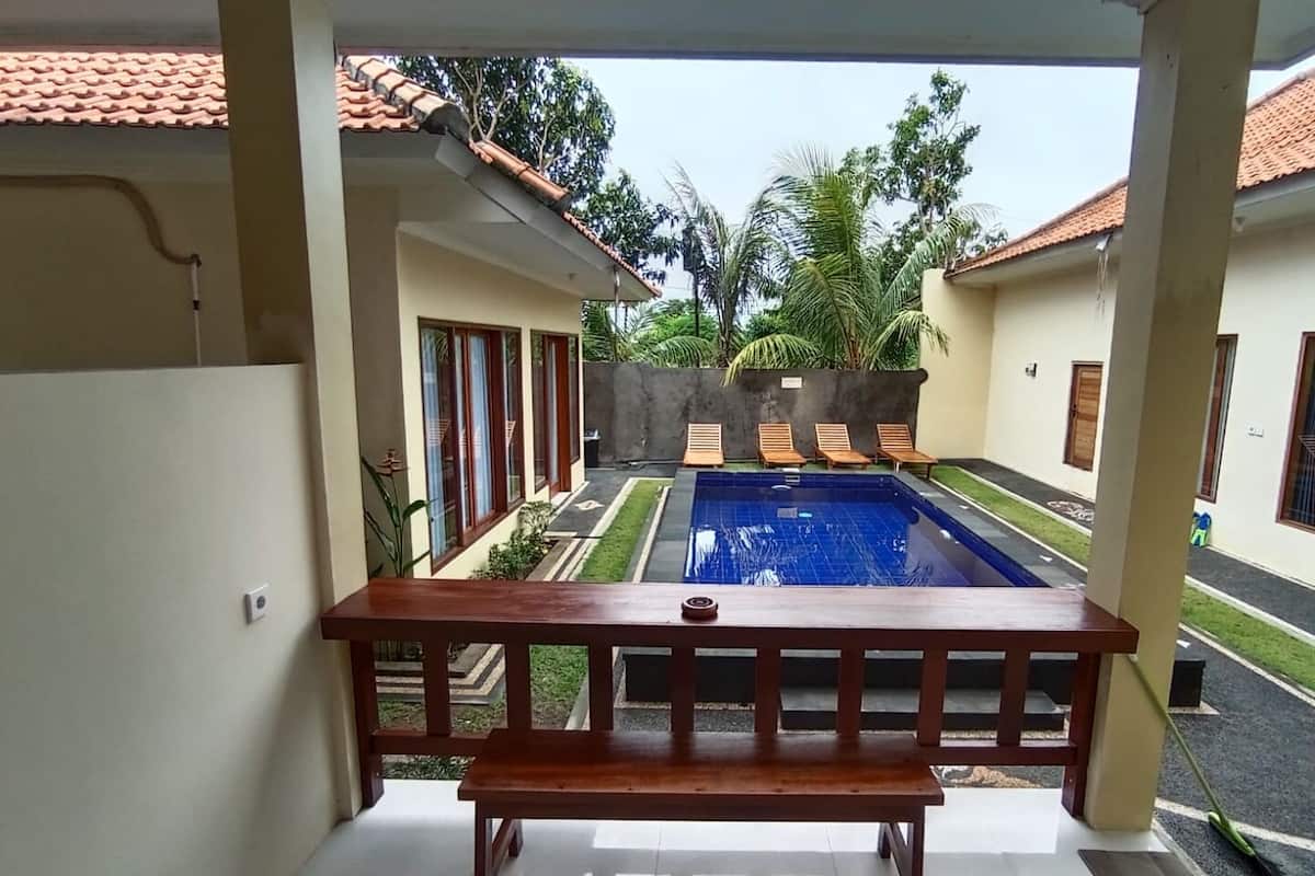 A view from a balcony overlooking a swimming pool with a tiled roof, palm trees, and lounge chairs.