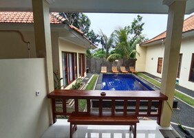A view from a balcony overlooking a swimming pool with a tiled roof, palm trees, and lounge chairs.