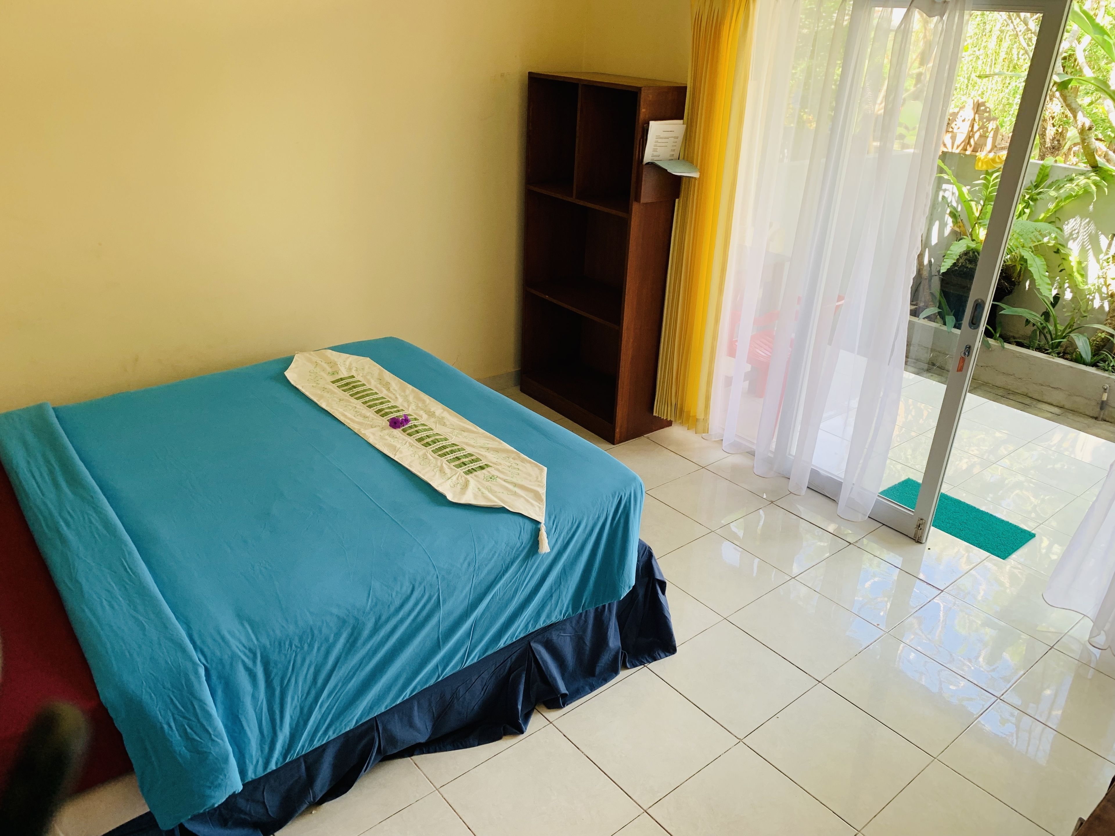 Quarto com cama, guarda-roupa de madeira e porta de vidro deslizante para uma varanda.