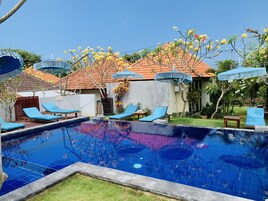 A swimming pool with blue tiles, surrounded by lounge chairs and umbrellas.