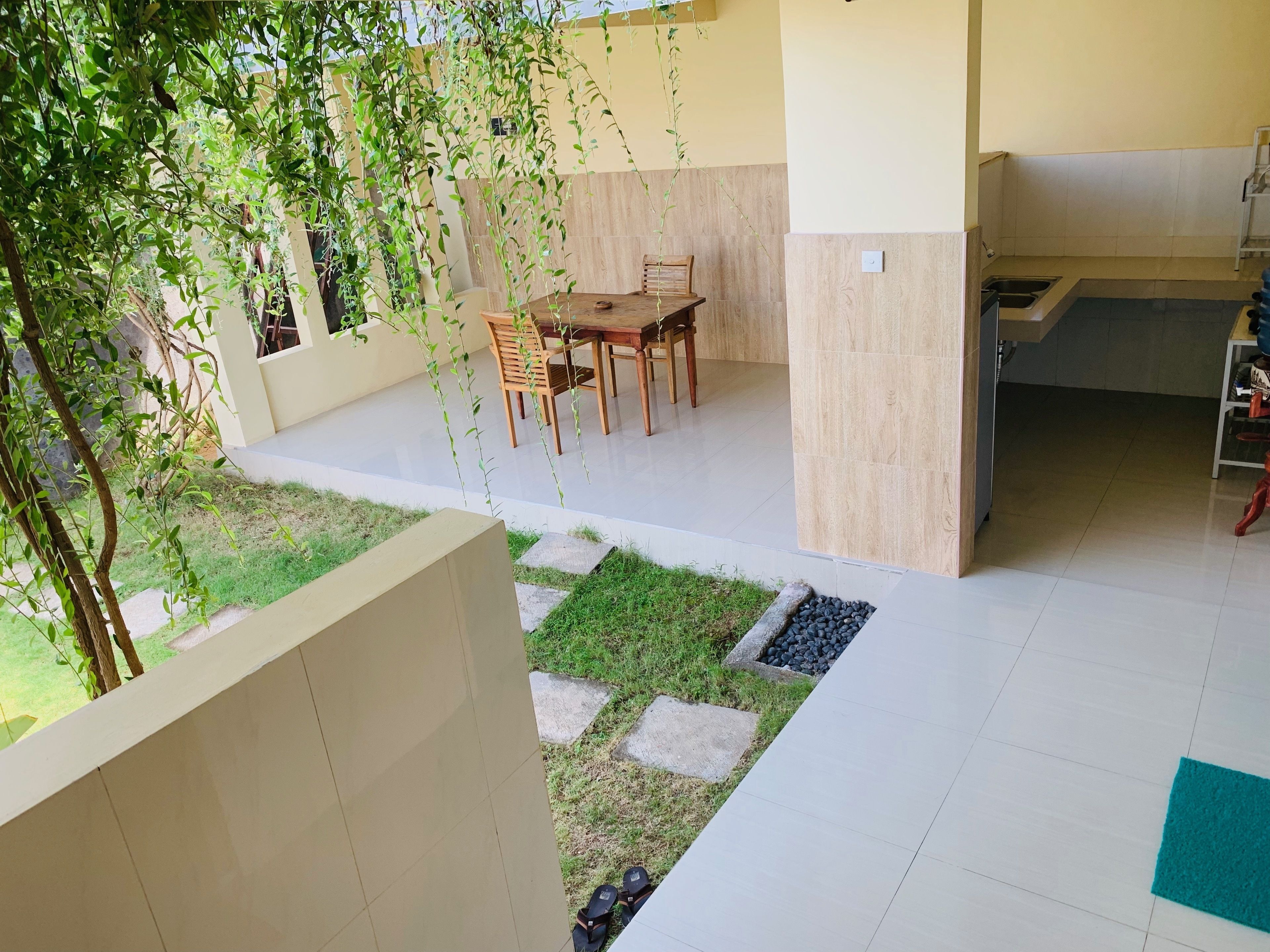 A modern outdoor patio with a wooden table and chairs, surrounded by a low stone wall and greenery.