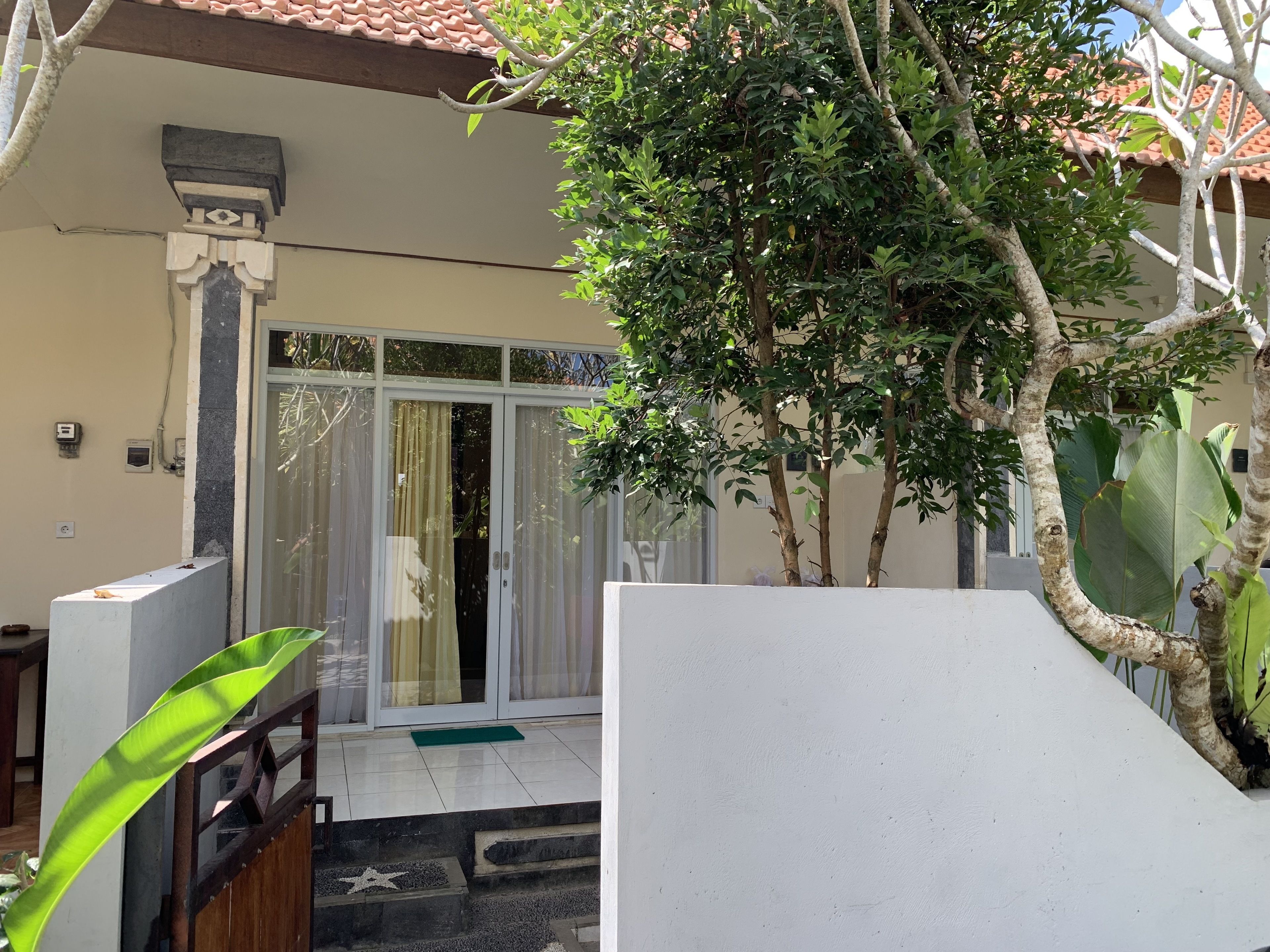 A residential property with a tiled roof, a sliding glass door entrance, a concrete block, and a green plant.