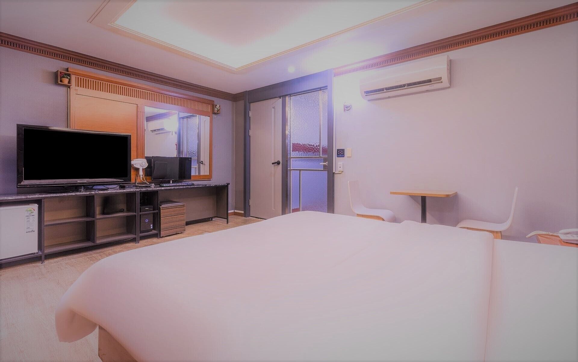 A hotel room with a bed, a desk with a computer, a television, and an air conditioning unit.