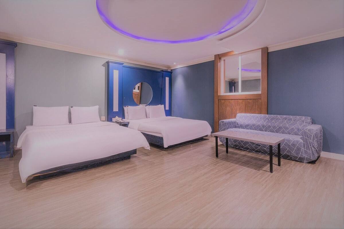Camera d'albergo con due letti, un divano, uno specchio e una plafoniera circolare.
