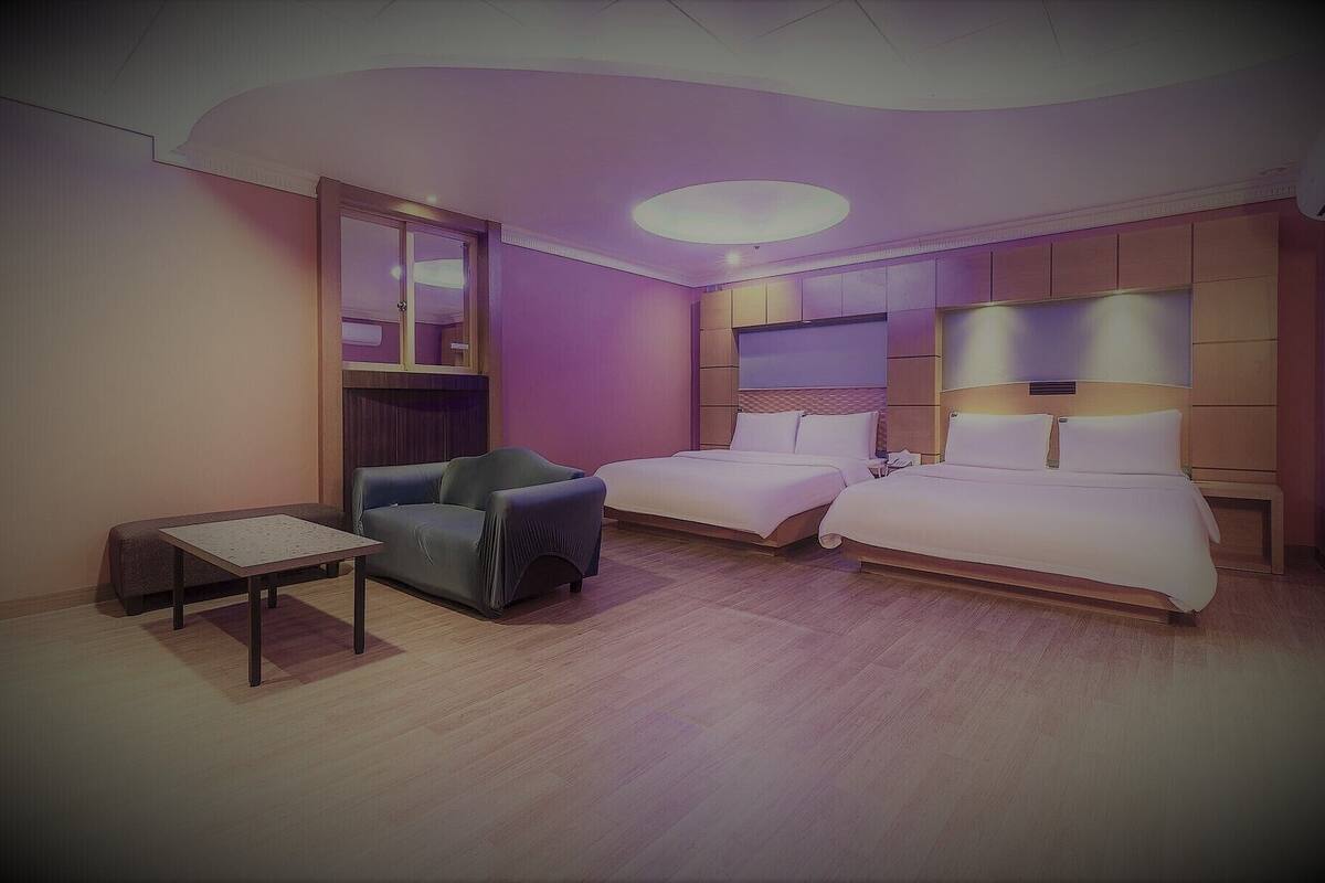 Una camera d'albergo con due letti, un tavolino, una sedia e uno specchio grande.