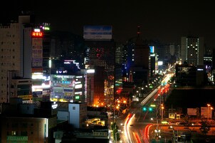 Un paisaje urbano nocturno con edificios iluminados y una calle concurrida.