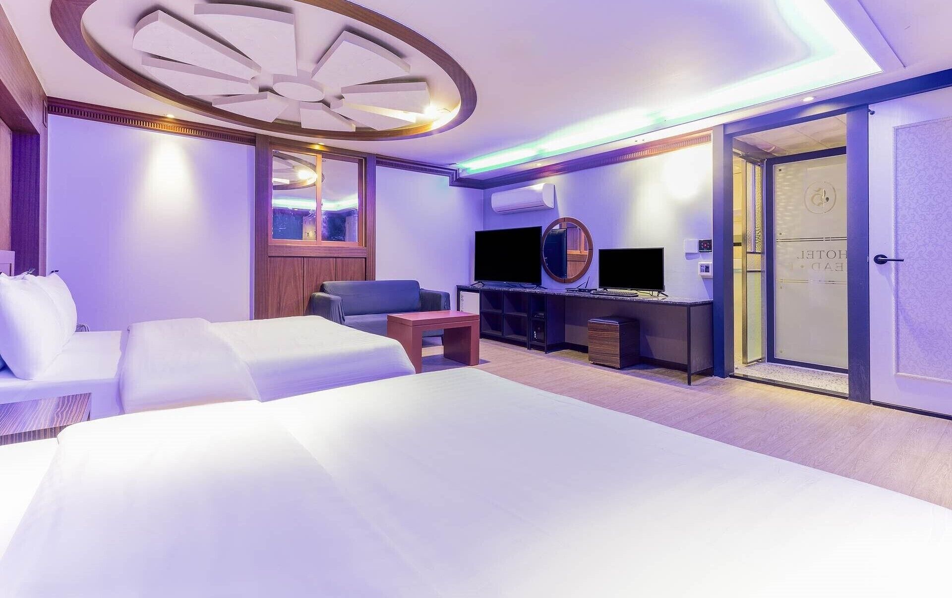 Una habitación de hotel moderna con una cama grande, una zona de estar con un sofá y sillones, un escritorio con ordenador y un televisor.