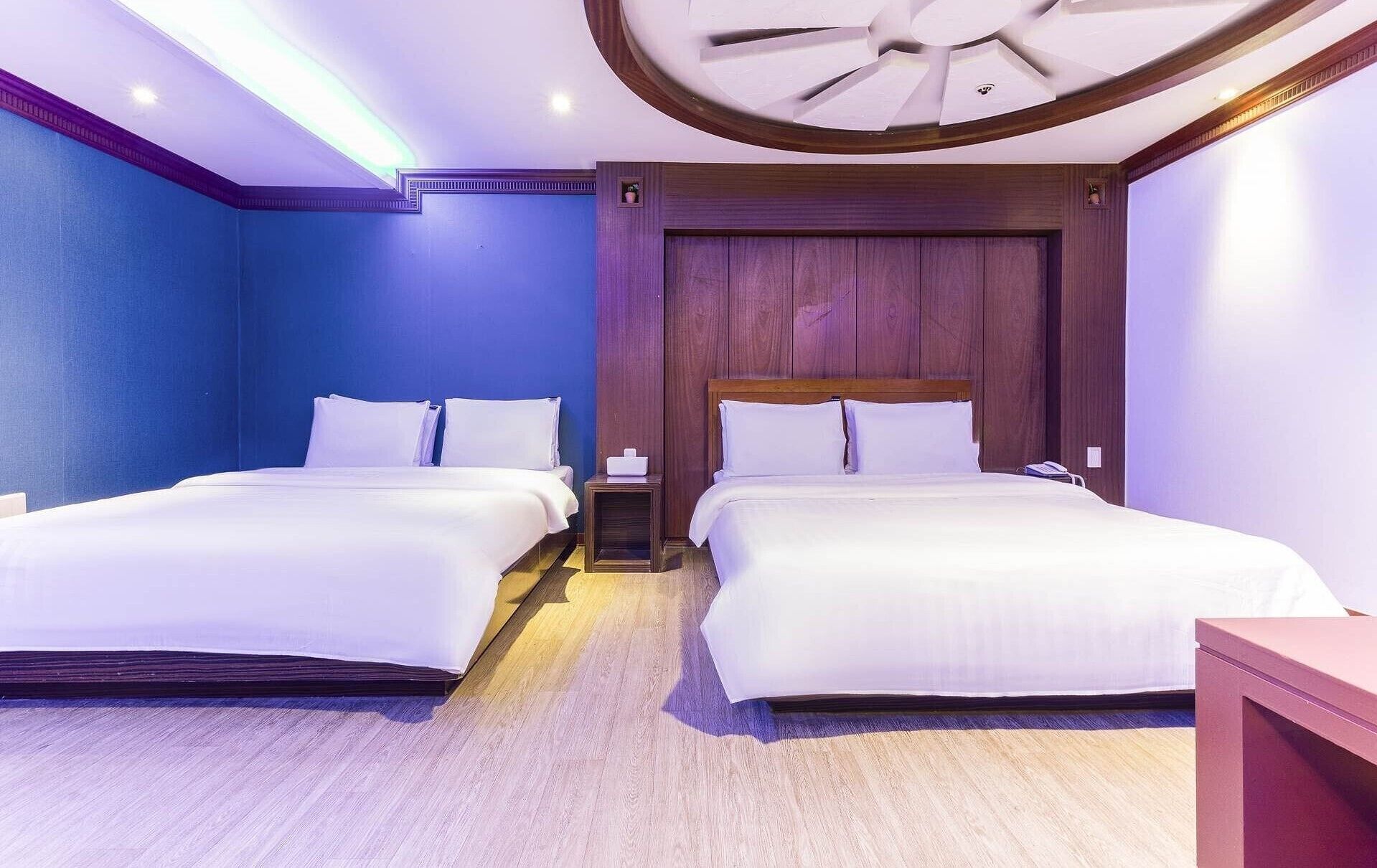 Habitación de hotel con dos camas, cabeceros de madera y un diseño moderno en el techo.