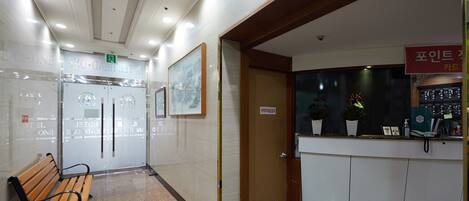 Un vestíbulo de hotel con una recepción, un banco de madera y una puerta que da a las habitaciones.