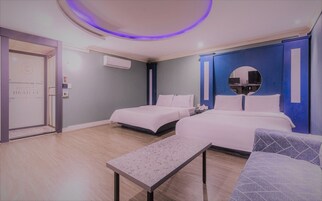 Habitación de hotel con dos camas, una mesita, un banco, un espejo redondo y un equipo de aire acondicionado.
