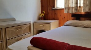 A bedroom with a bed, a nightstand, a dresser, and a window with curtains.