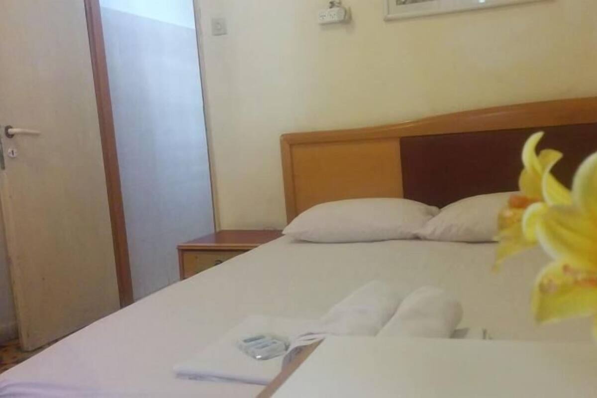 A hotel room with a bed, a nightstand, a door, and a wall-mounted light fixture.