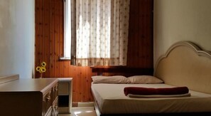 A bedroom with wooden walls, a bed with white and red bedding, a dresser, and a window with patterned curtains.