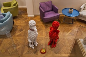 A room with a wooden parquet floor, a white poodle sculpture, a red sculpture, and a small red bowl.