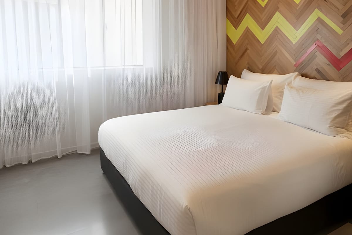 Un dormitorio moderno con una cama grande, cortinas translúcidas, un muro con diseño de greca y una obra de arte en el techo.