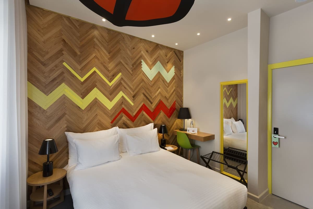 Una habitación de hotel moderna con una cama grande, un escritorio, una silla, una lámpara y un espejo.