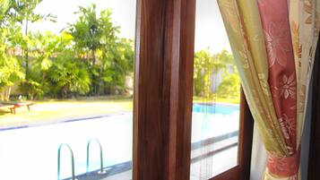 A view through a window with a pool, a wooden frame, and curtains.