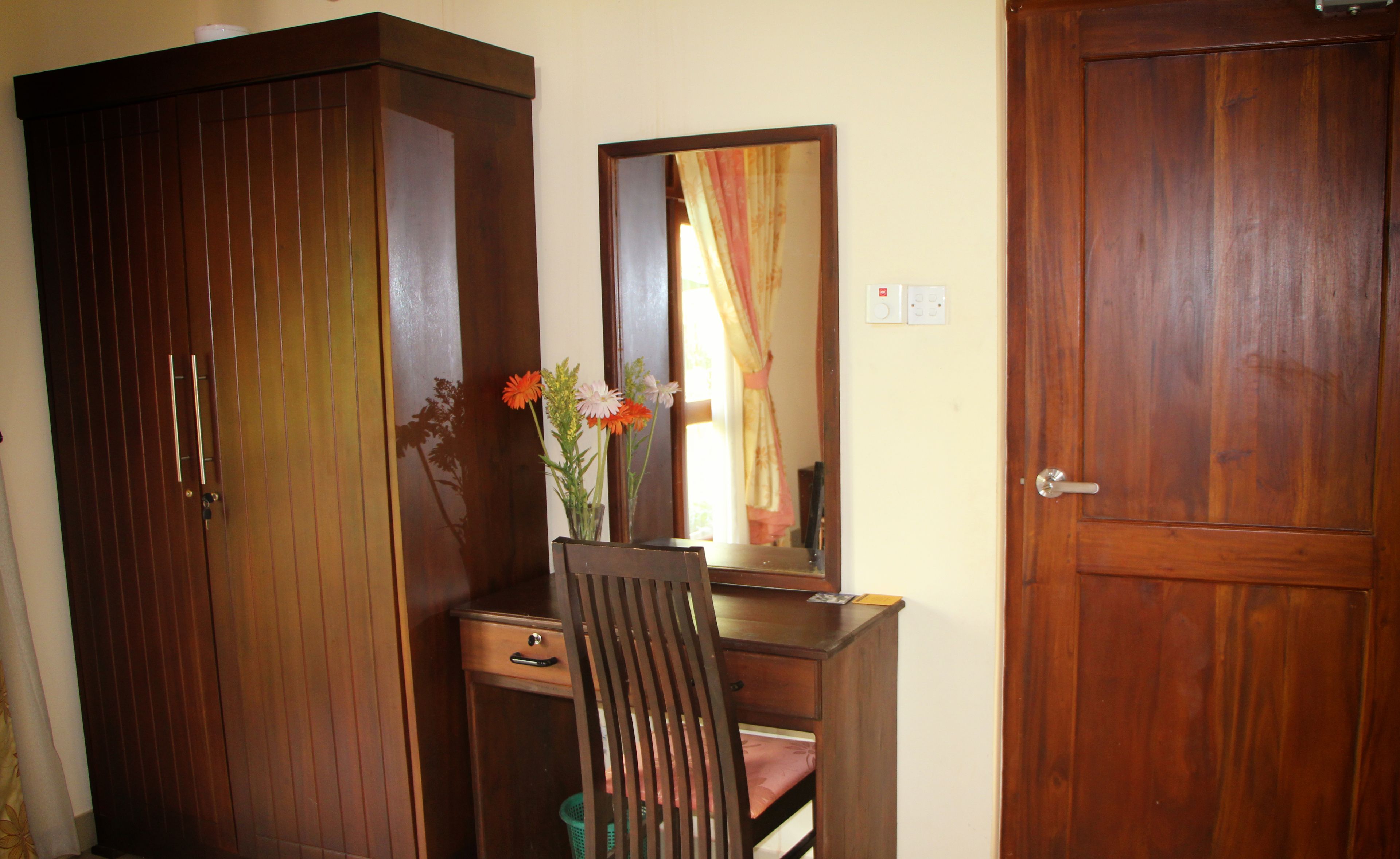 A room with a wooden wardrobe, a mirror, and a desk with a chair.