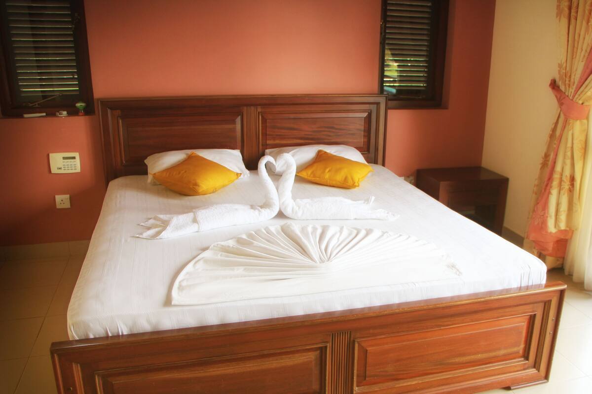 Una cama bien tendida con un diseño de cisne y pato, dos almohadas amarillas y un cabecero de madera.