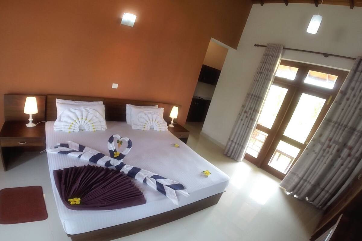 Una habitación de hotel con una cama grande, dos mesitas de noche con lámparas, una ventana con cortinas y vistas al exterior.